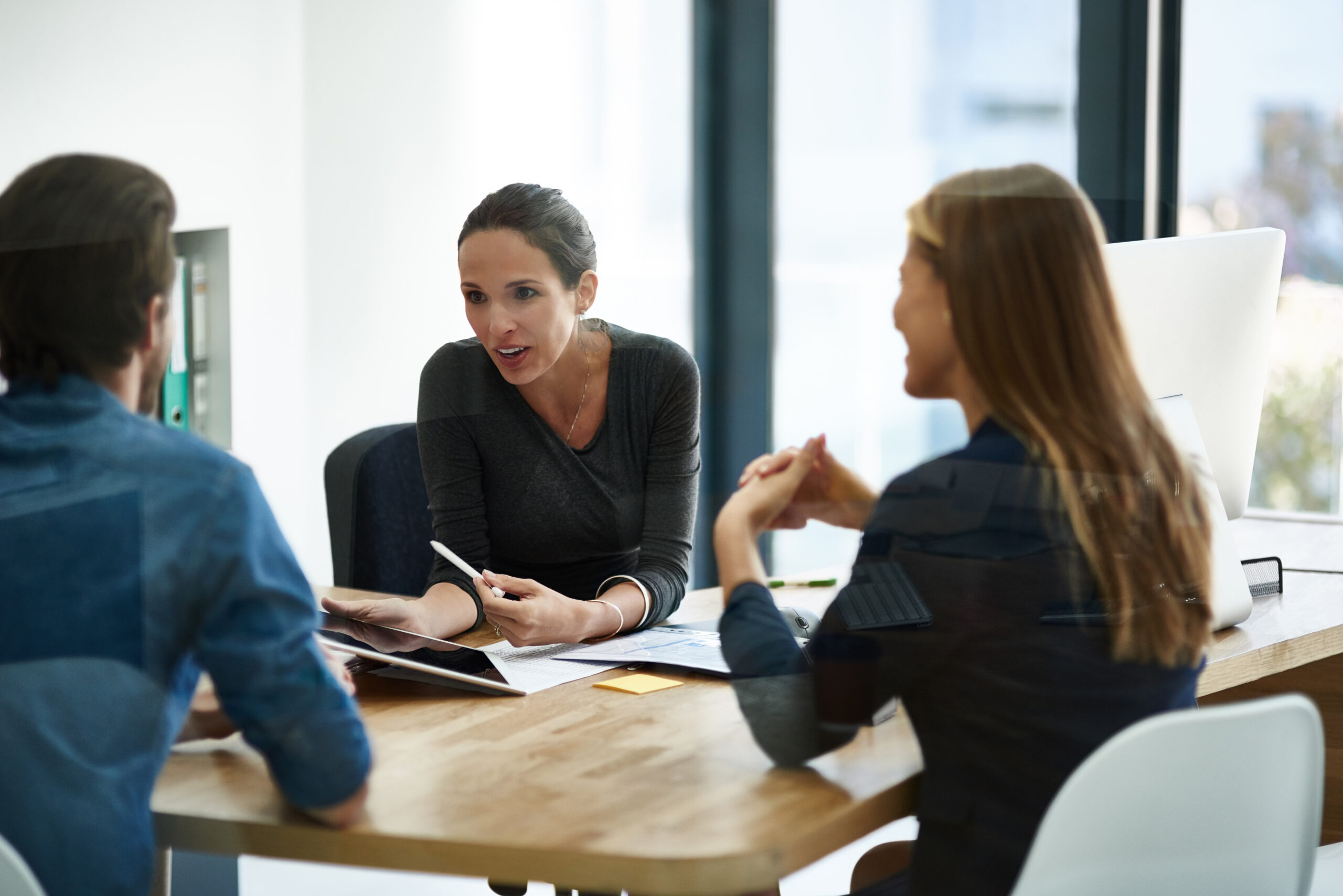 Three employees discuss a digital compliance form during a management meeting at AAPA.