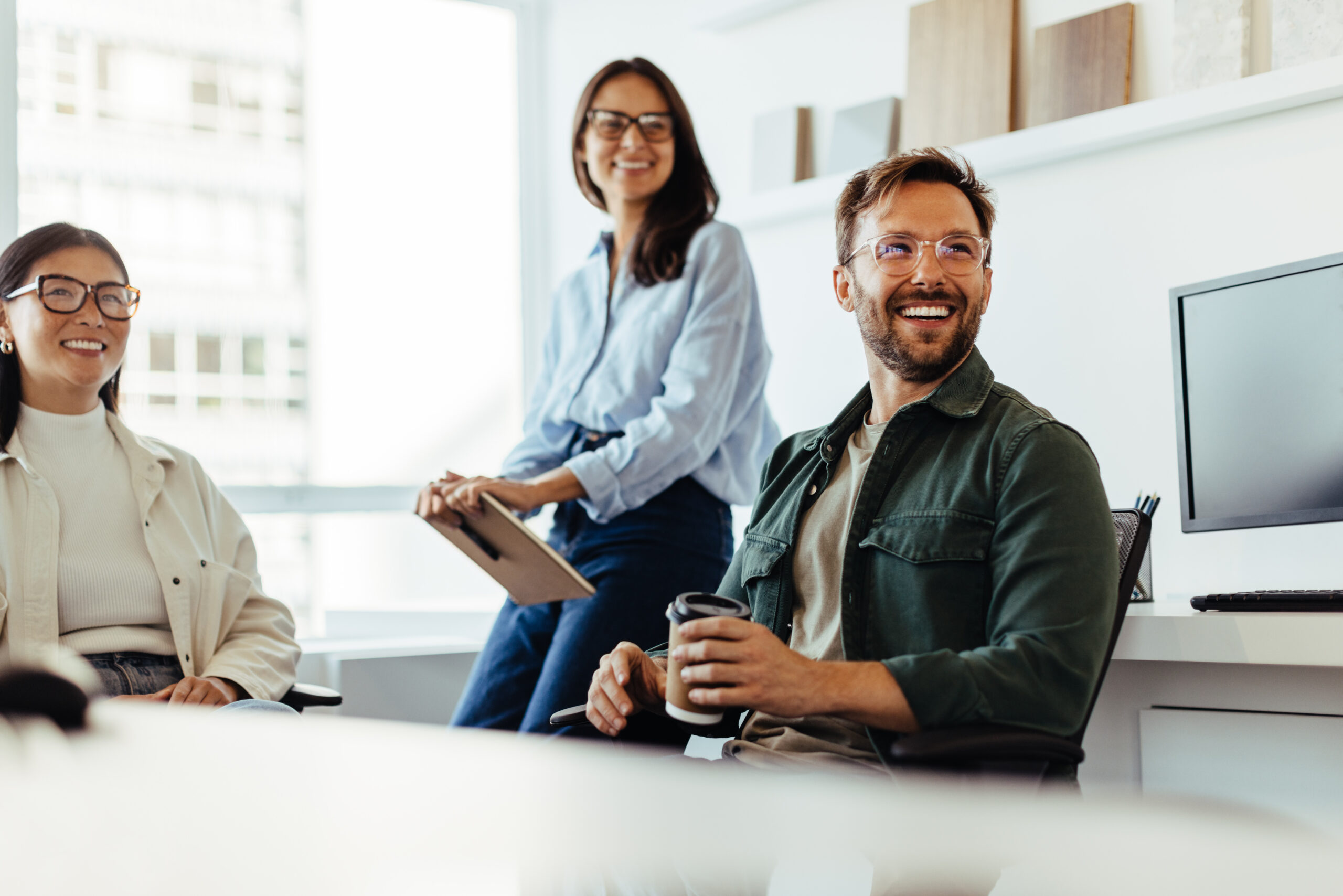 Three professionals collaborate in a bright office setting, with one holding a tablet device.