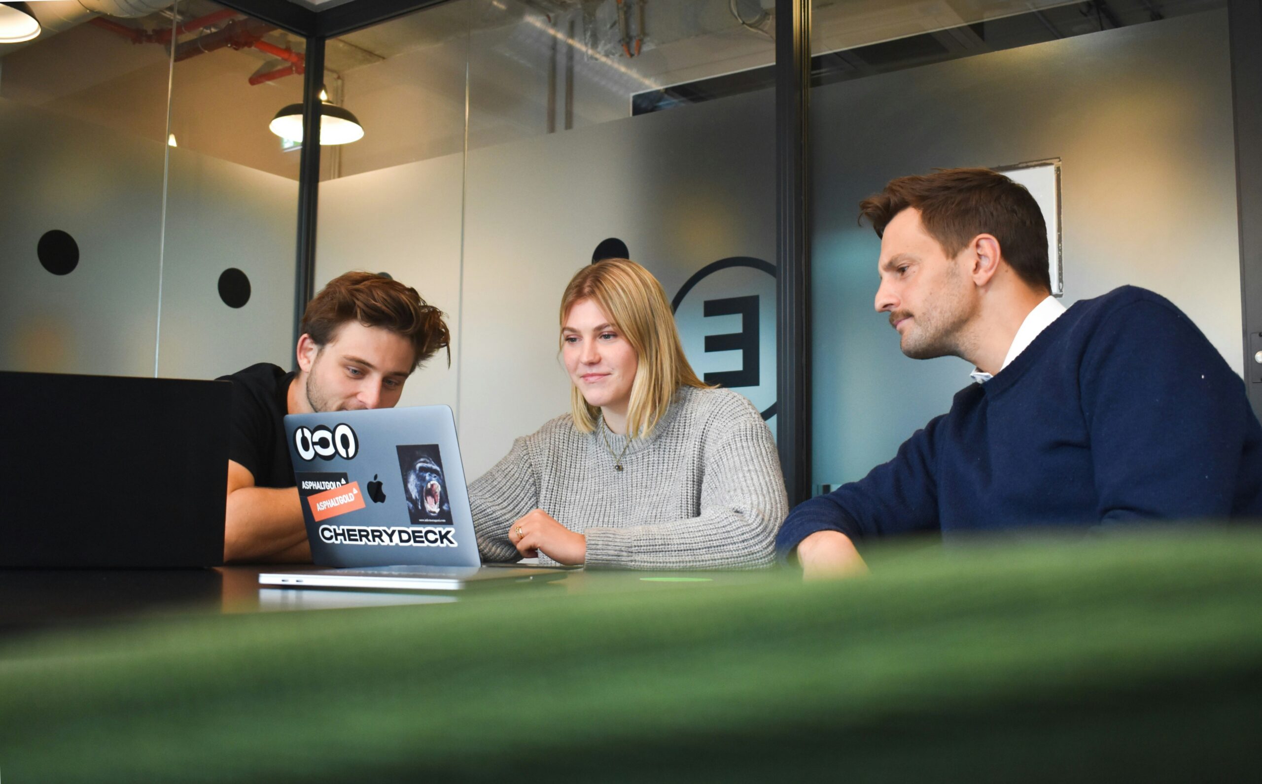 Cherrydeck Unsplash — three colleagues sit at a table in a modern office looking at a laptop screen during a meeting at AAPA.