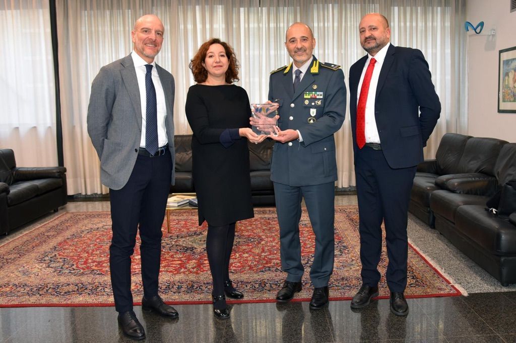 Quatre personnes en tenue officielle présentent un prix en cristal lors d'une cérémonie en intérieur.